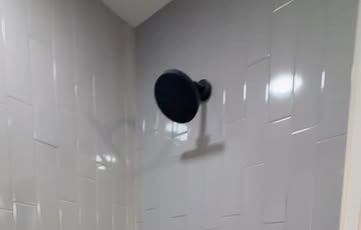 Tile shower wall with a matte-black shower head, from a primary en-suite tub-to-walk-in-shower conversion in a four-bedroom North Austin home